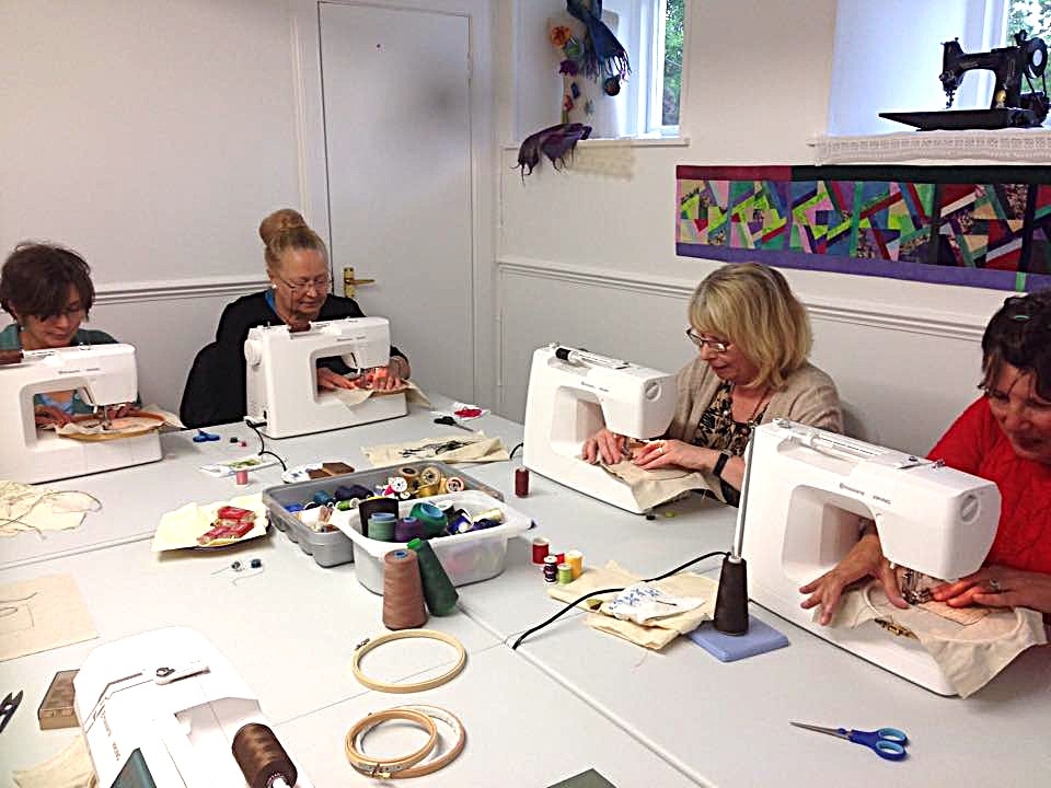 Students working at sewing machines during a free‑motion embroidery workshop, surrounded by colourful threads and textile materials.