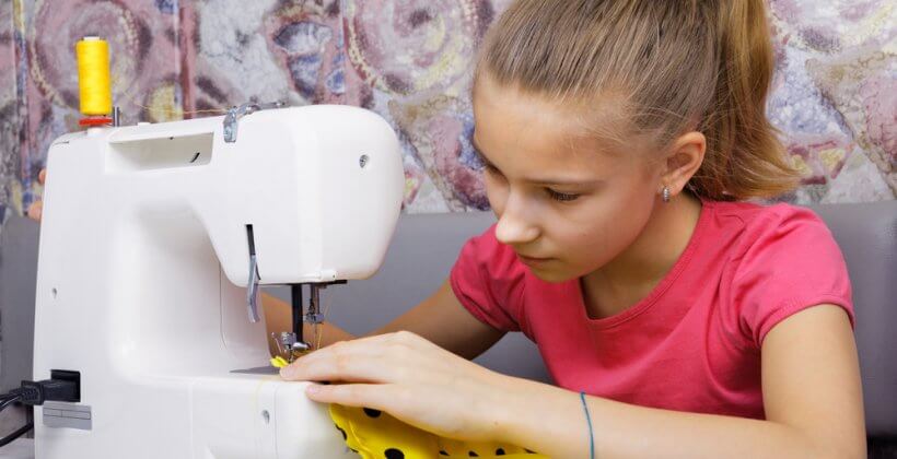 Kids sewing course. A young girls sits at a sewing machine using yellow spotted fabric