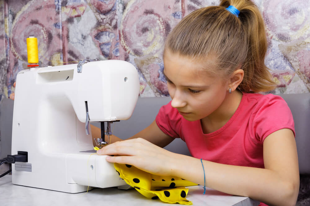 Kids sewing course. A young girls sits at a sewing machine using yellow spotted fabric