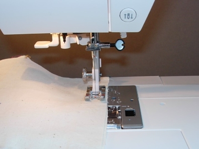 Close‑up of a sewing machine needle, presser foot and seam guide markings while stitching fabric