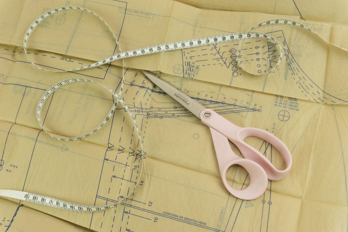Dressmaking techniques - image shows a paper dressmaking pattern, pink fabric shears and a tape measure