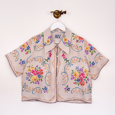 Image shows a ladies shirt made from a vintage embroidered tablecloth. The fabric is linen in a soft beige colour with bright floral hand embroidery covering the shirt.