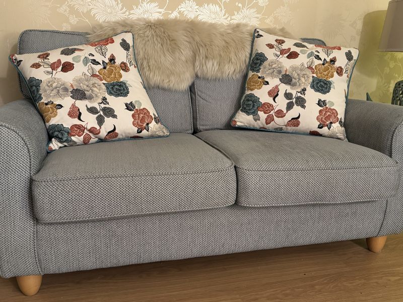 Two floral-print cushions with a cream background placed on a duck-egg colour sofa.
