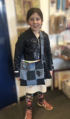 A girl stands in a sewing studio proudly wearing her patchwork crossbody bag she has made from jeans.