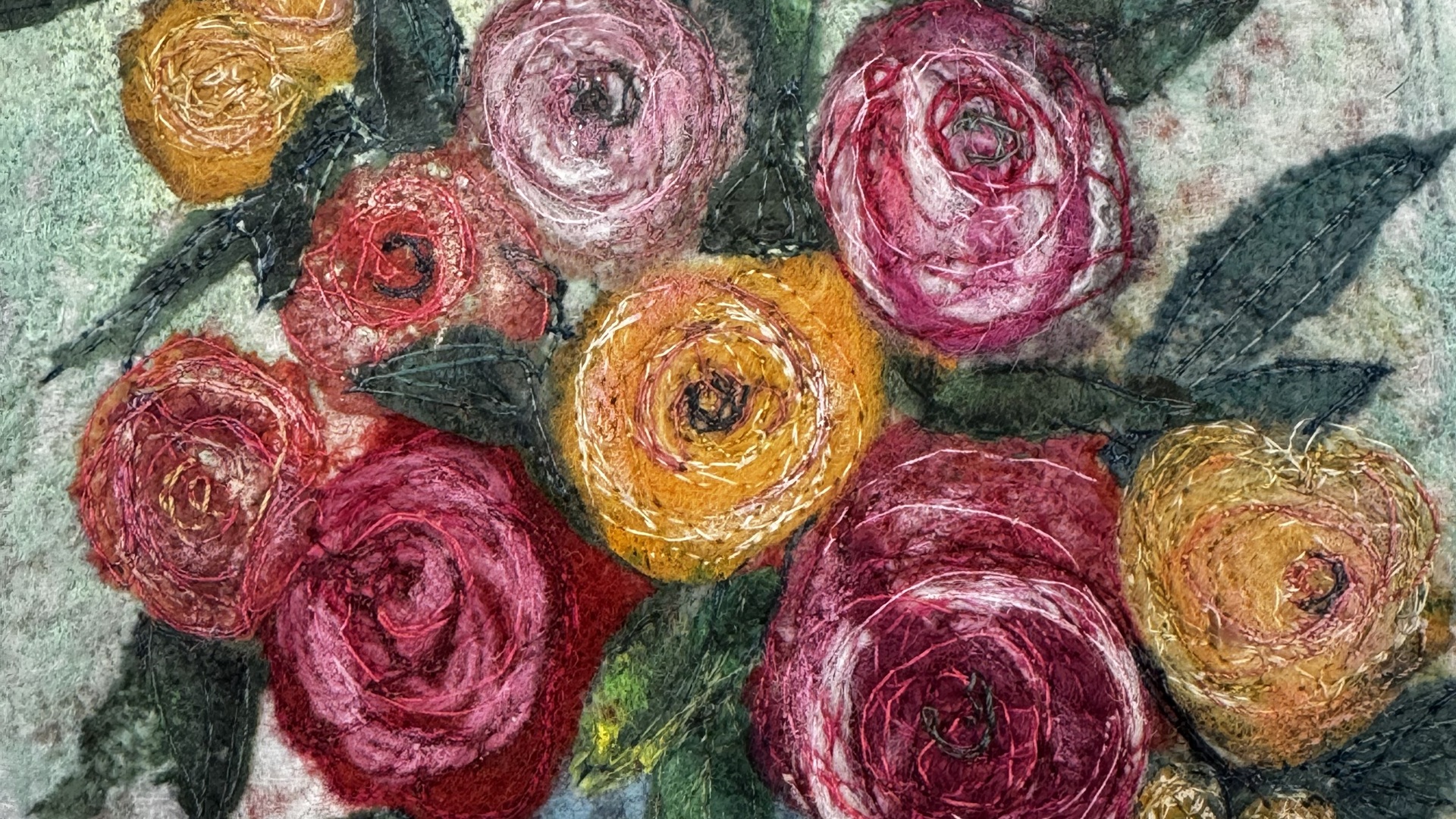 A colourful bouquet of flowers created from needle-felted roses and free-motion stitching. The flowers are in tones of red, deep pink and yellows, with dark green leaves and a pale aqua background